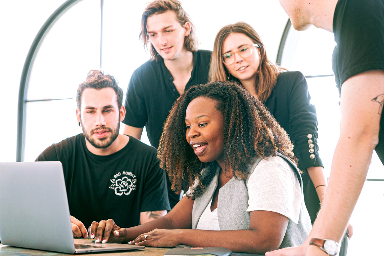Diverse team of five young professionals collaborating around a laptop in a modern office setting.